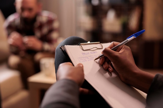 Psicólogo masculino tomando notas en la sesión de terapia de pareja para ayudar con problemas de relación, consejero dando consejos. Explicando problemas matrimoniales, usando papel para hacer psicoanálisis. De cerca,