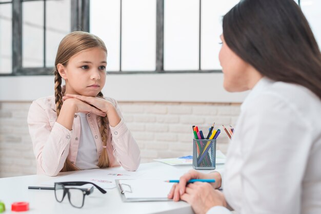Psicólogo del niño joven que habla con la niña triste en la oficina