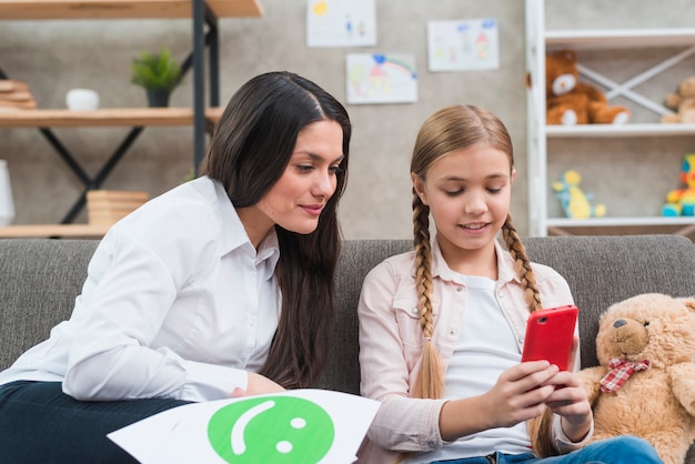 Psicólogo del niño joven que mira el asimiento del teléfono móvil por la niña