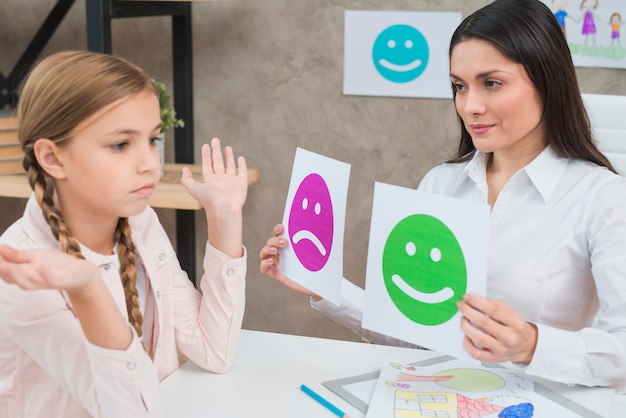 El psicólogo sonriente que muestra la emoción feliz y triste hace frente a tarjetas a la niña