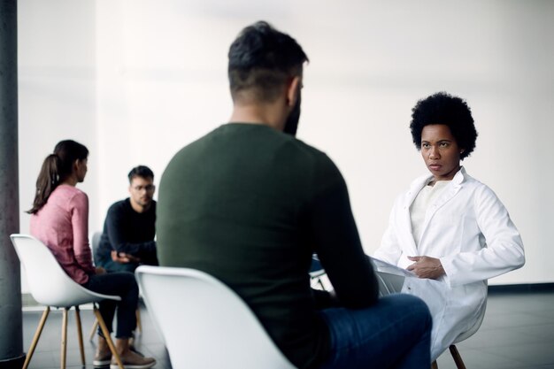 Psicoterapeuta afroamericano hablando con un paciente masculino durante la terapia de grupo