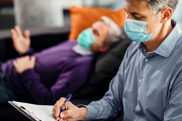 Psiquiatra tomando notas mientras asesora a un paciente durante la pandemia de coronavirus