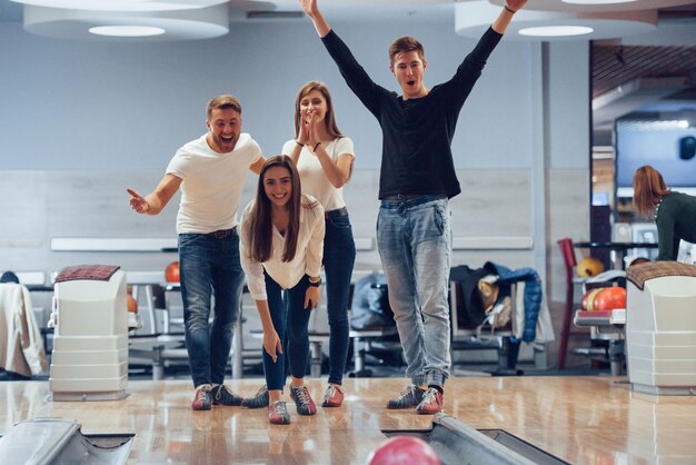 Puedes hacer la huelga. Jóvenes amigos alegres se divierten en el club de bolos en sus fines de semana