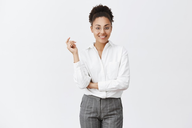 Puedo ocuparme de tus problemas. Retrato de joven empleada inteligente y creativa con gafas y camisa, sosteniendo la mano cruzada sobre el pecho y levantando un brazo en pose confiada y atrevida, sonriendo