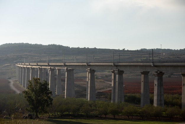 Puente de hormigón en un campo rodeado de vegetación con colinas en el fondo