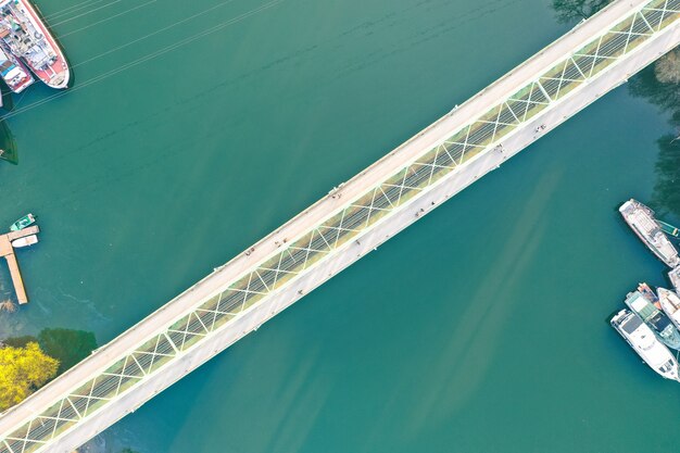 Puente largo y estrecho que cruza un gran río con barcos atracados en la costa