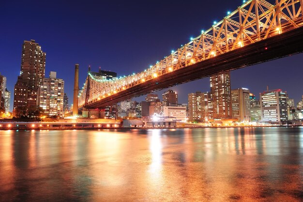 Puente de Queensboro sobre el East River de la ciudad de Nueva York al atardecer con reflejos del río y el horizonte del centro de Manhattan iluminado.