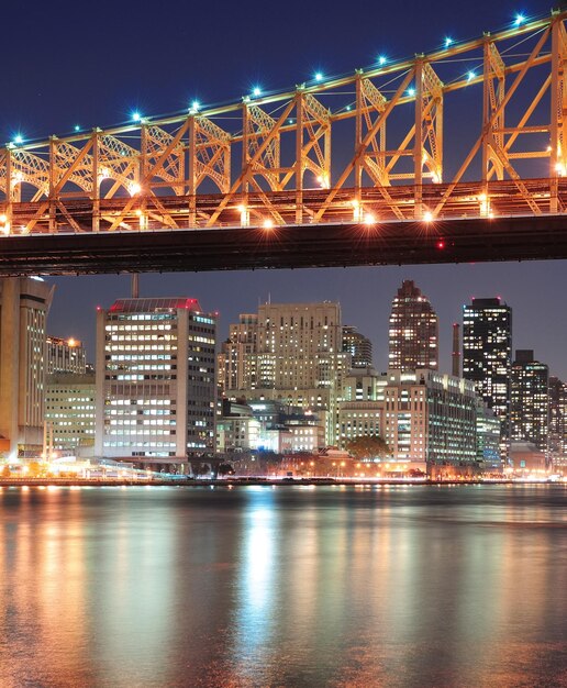 Puente de Queensboro sobre el East River de la ciudad de Nueva York al atardecer con reflejos del río y el horizonte del centro de Manhattan iluminado.