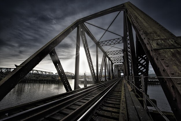 Puente Vierendeel con vías de tren cerca del lago y el impresionante sol que brilla en el cielo oscuro