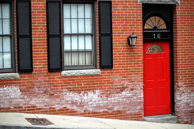 Puerta de entrada roja a un edificio de ladrillo que muestra el número dieciséis en una calle con ventanas de vidrio