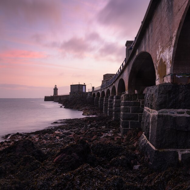 Puesta de sol en el cielo sobre el puente y el faro junto al mar en Guernsey