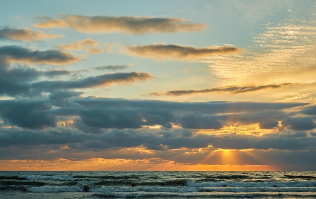 Puesta de sol sobre el mar con nubes coloridas, luz solar naranja, los rayos del sol brillan a través de las nubes, la idea de un fondo o una pantalla de inicio