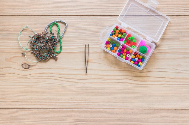 Pulsera; pinzas y caja de granos coloridos en la mesa