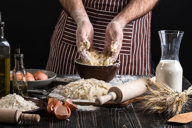 Un puñado de harina con huevo en una cocina rústica. En el contexto de las manos de los hombres amasar la masa. Ingredientes para cocinar productos de harina o pan de masa, magdalenas, pasteles, masa de pizza. copia espacio