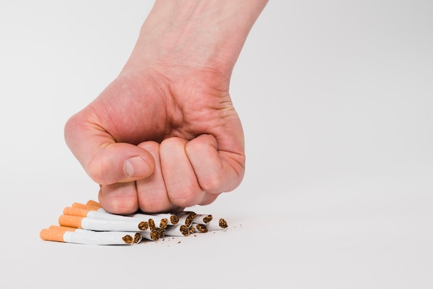 Un puño persona aplastando cigarrillos aislados sobre fondo blanco