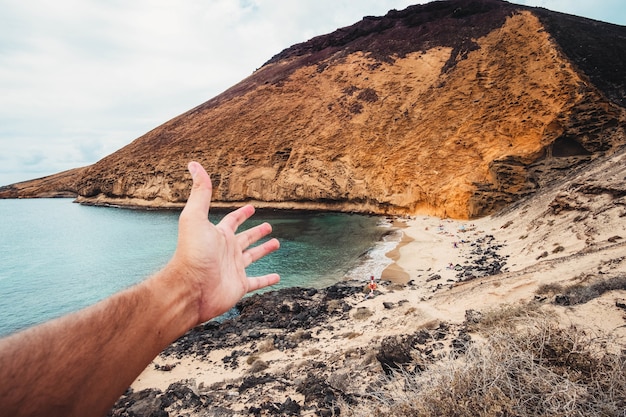 Punto de vista de la foto de una mano masculina que se extiende hacia la costa rocosa de Playa Amarilla, España