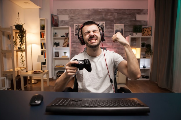 Punto de vista de un joven feliz celebrando su victoria en un juego de disparos en línea con un controlador inalámbrico.