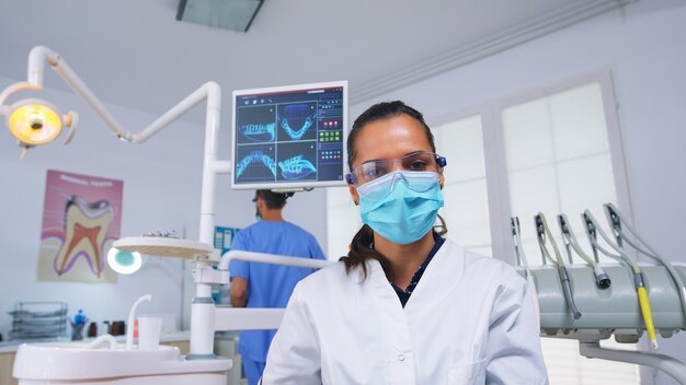 Punto de vista del paciente al estomatólogo que pone máscara de oxígeno antes de la cirugía dental sentado en una silla estomatológica. Médico y enfermera que trabajan en la oficina de ortodoncia moderna con guantes y máscara de protección