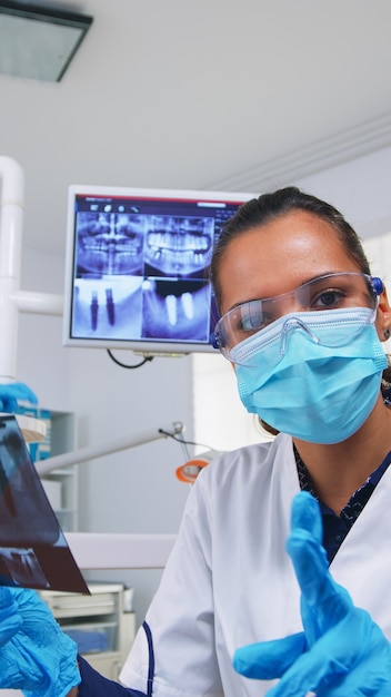 Foto gratuita punto de vista del paciente mirando al dentista pidiendo una radiografía dental que muestre la imagen de los dientes. especialista en estomatología con máscara protectora, trabajando en la clínica estomatológica moderna, explicando la radiografía del diente