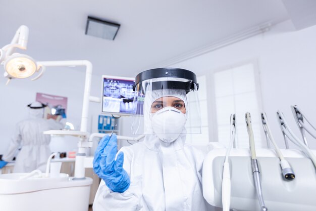 Punto de vista del paciente sentado en una silla en el consultorio dental para el tratamiento de los dientes Estomatólogo con equipo de seguridad contra el coronavirus durante el control de la atención térmica del paciente.