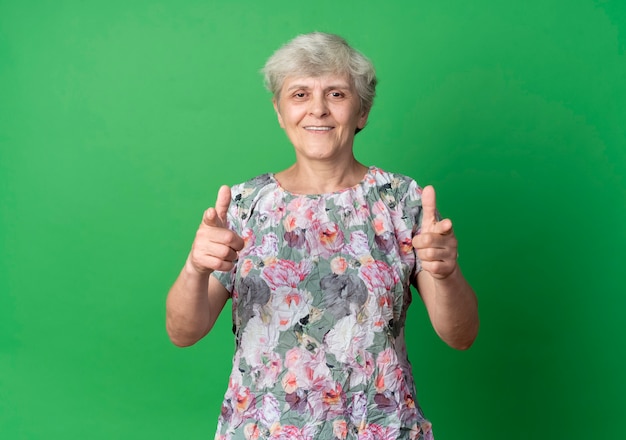 Puntos de anciana sonriente con las dos manos aisladas en la pared verde