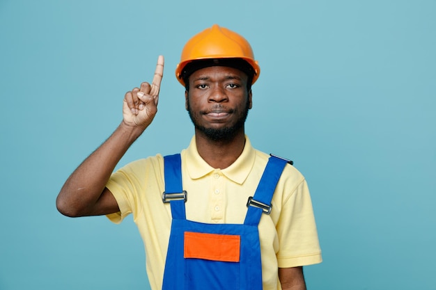 Puntos impresionados en el joven constructor afroamericano en uniforme aislado sobre fondo azul.