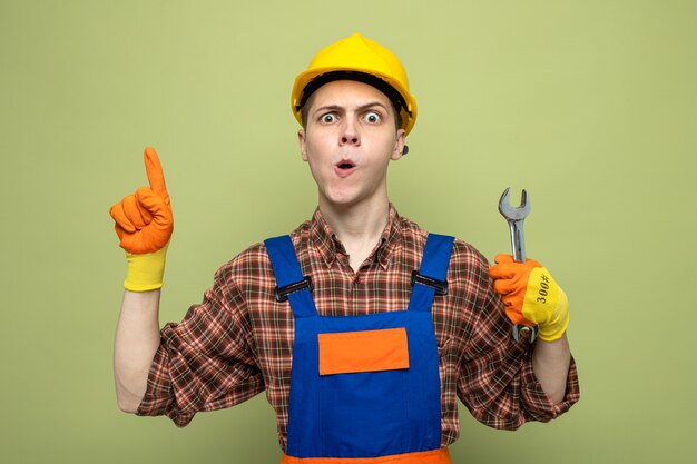 Puntos impresos en el constructor masculino joven vistiendo uniforme con guantes sosteniendo una llave de boca