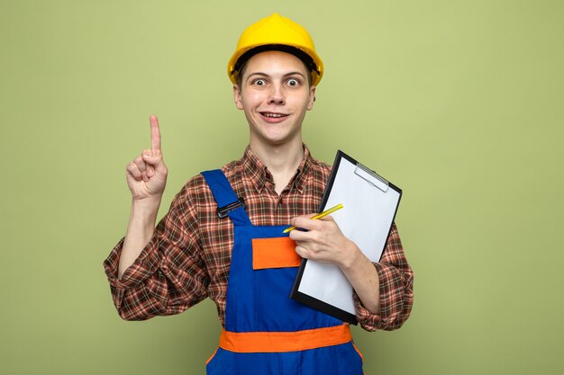 Puntos impresos en el joven constructor de sexo masculino sosteniendo el portapapeles vistiendo uniforme