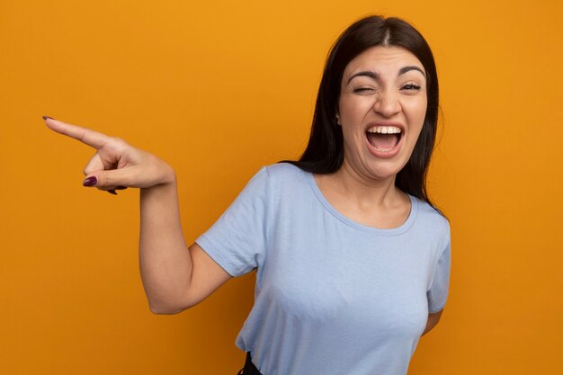 Puntos de mujer morena bonita alegre al lado aislado en la pared naranja