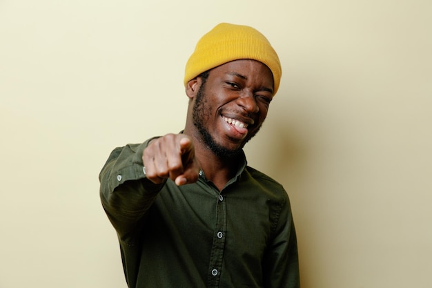 Puntos de risa en la cámara joven afroamericano con sombrero con camisa verde aislada sobre fondo blanco