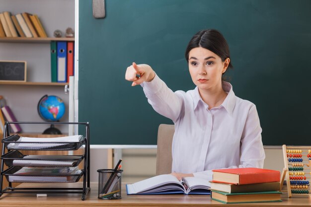 puntos seguros al lado joven maestra sentada en el escritorio con herramientas escolares en el aula