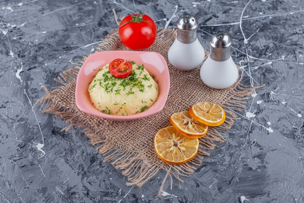 Puré de papas en un recipiente junto a sal, limón y tomates sobre una arpillera, sobre la mesa azul.