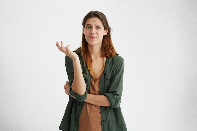 Foto gratuita ¿qué? mujer desconcertada vestida de manera informal de pie en la pared en blanco, con una mirada cuestionable, sus emociones faciales y gestos que expresan indignación, disgusto e incertidumbre hacia algo