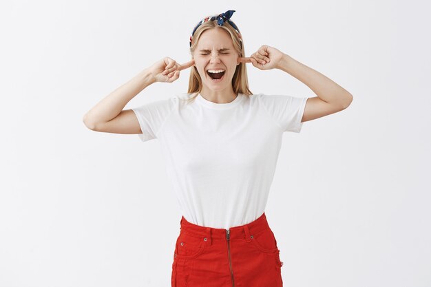 Quejarse molesta joven rubia posando contra la pared blanca