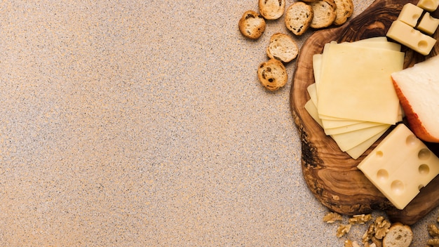 Queso emmental y queso gouda con rebanadas en posavasos con rebanadas de pan y nogal sobre fondo texturado beige