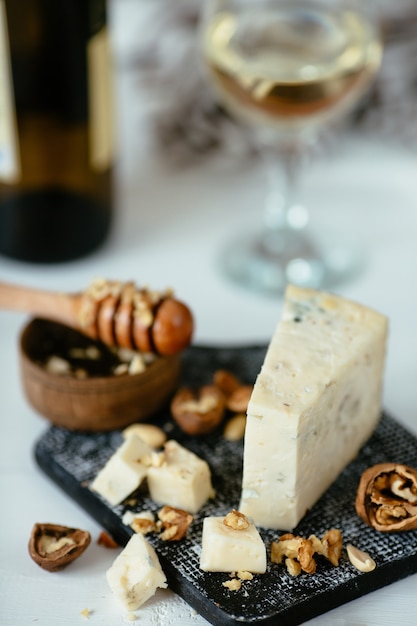 Queso gorgonzola azul italiano sobre una mesa de madera con miel, nueces y vidrio