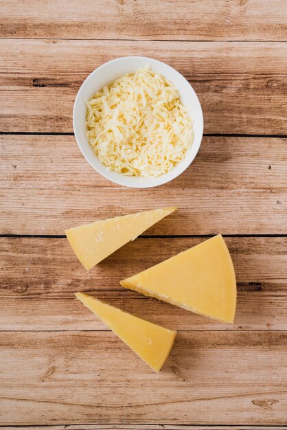 Queso rallado y triangular en mesa de madera.