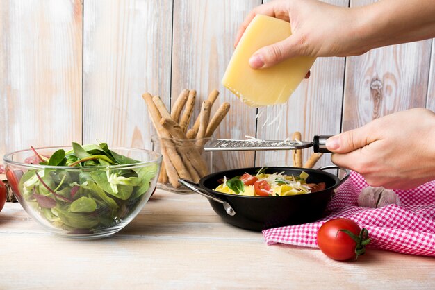 Queso de rejilla de la mano de la persona sobre la pasta en cocina