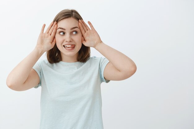 Quien no se esconde corre. Retrato de divertida y divertida joven encantadora juguetona en camiseta azul claro sacando la lengua de la emoción jugando a escondidas y mirando a la derecha con expresión emocionada