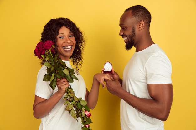 Quieres casarte conmigo. Celebración del día de San Valentín, feliz pareja afroamericana aislada sobre fondo amarillo de estudio. Concepto de emociones humanas, expresión facial, amor, relaciones, vacaciones románticas.