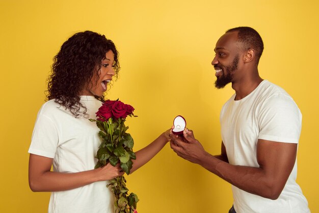 Quieres casarte conmigo. Celebración del día de San Valentín, feliz pareja afroamericana aislada sobre fondo amarillo de estudio.