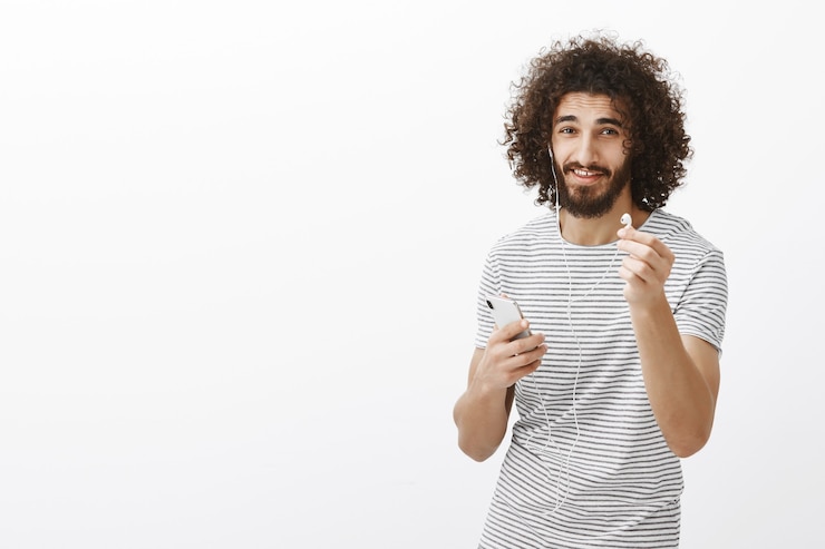 Foto gratuito quiero compartir auriculares. modelo masculino delgado y atractivo amigable en camiseta a rayas, tirando del auricular hacia y sosteniendo el teléfono inteligente