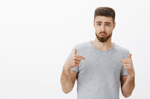 Quiero tener un cuerpo tan perfecto. Hombre guapo seguro de sí mismo con barba elegante y peinado apuntando a sí mismo cuestionado y decidido a sentirse seguro recomendando un programa de nutrición para el visitante del gimnasio