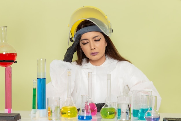 Química femenina de vista frontal en traje de protección especial trabajando con soluciones y con dolor de cabeza en la superficie verde