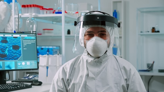 Foto gratuita químico con exceso de trabajo sentado en un moderno laboratorio equipado con un mono mirando cansado a la cámara. equipo de médicos que examinan la evolución del virus utilizando herramientas de alta tecnología y química para el desarrollo de vacunas