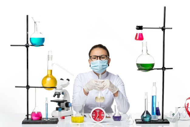 Químico femenino de vista frontal en traje médico blanco con solución de sujeción de máscara sobre fondo blanco laboratorio químico virus covid- splash