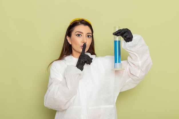 Químico femenino de vista frontal en traje de protección especial con matraz con solución sobre la superficie verde claro