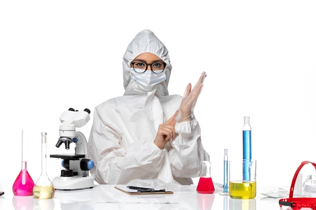 Químico femenino de vista frontal en traje de protección especial sentado con soluciones sobre fondo blanco química virus covid pandémico