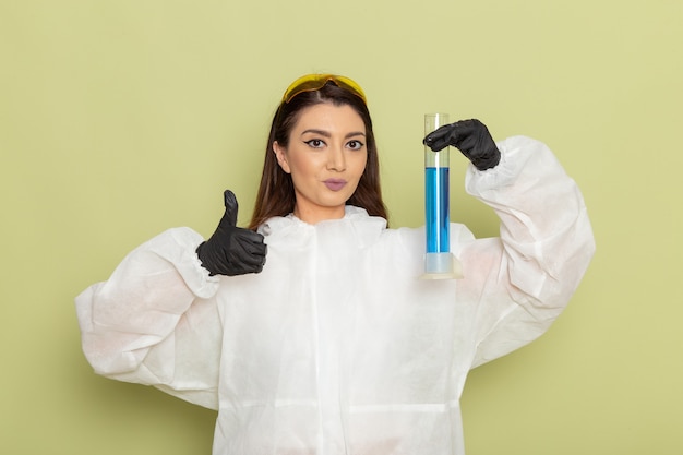 Químico femenino de vista frontal en traje de protección especial sosteniendo el matraz con solución azul y posando sobre una superficie verde