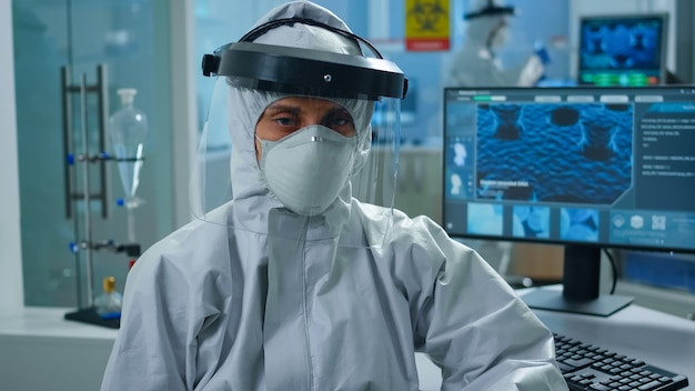 Químico de la mujer con exceso de trabajo sentado en el laboratorio equipado moderno vistiendo un mono mirando cansado en la parte delantera